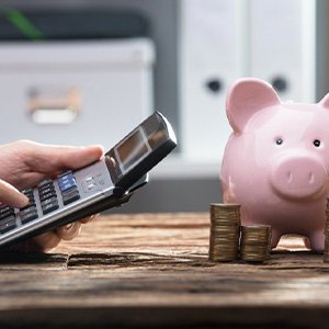 Hands operate a pocket calculator near a piggy bank