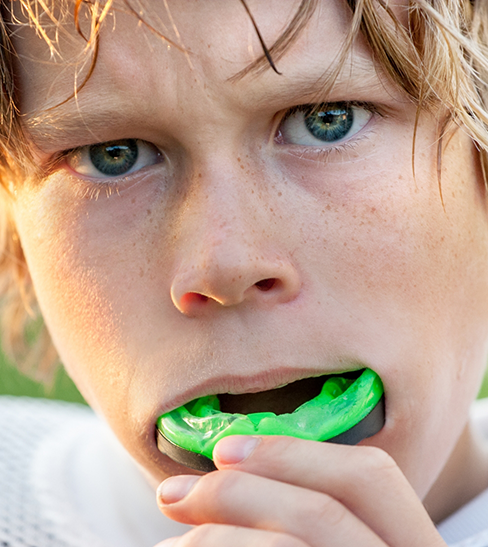 Young boy putting in a green mouthguard