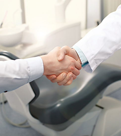 Patient and dentist shaking hands in front of dental chair