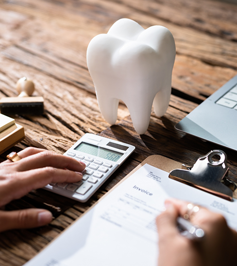 Filling out form on clipboard with calculator and tooth-shaped paperweight nearby