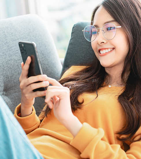 Woman with glasses lying on couch and looking at phone